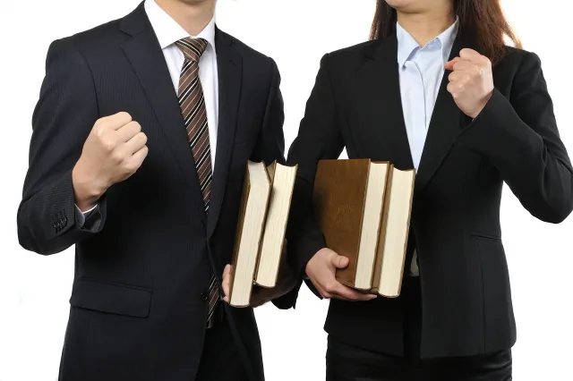 スーツ姿で本を持ちガッツポーズをしている男女
