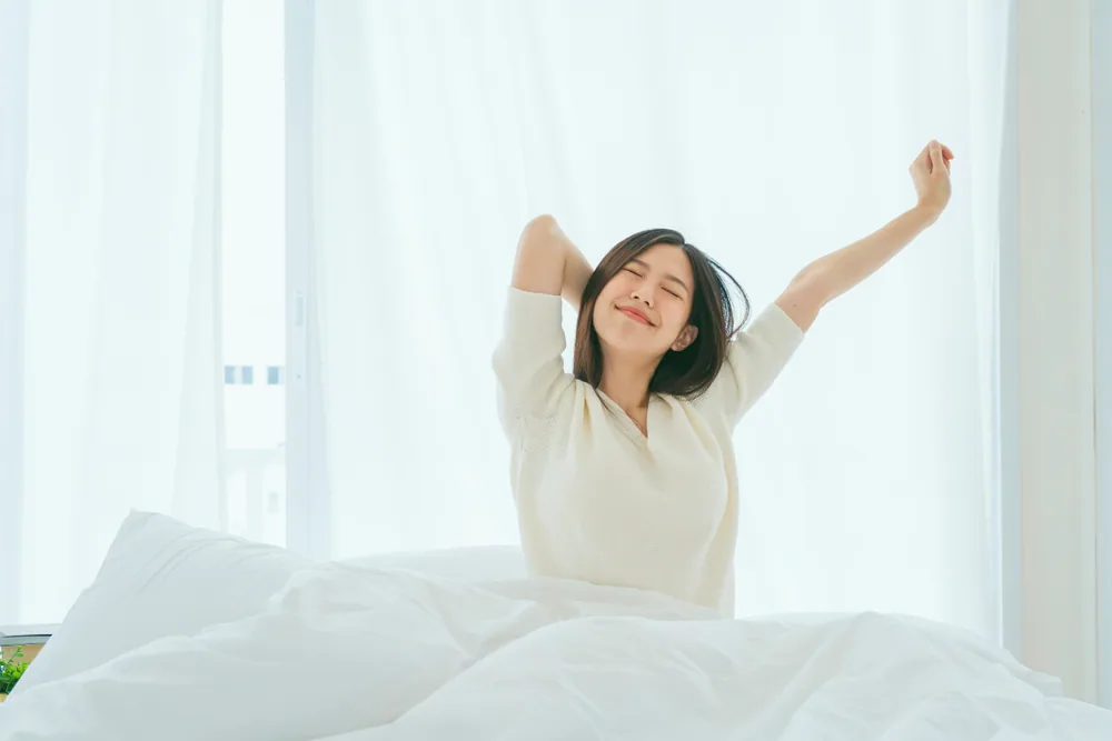 ベッドの上で気持ちよさそうに背伸びをしている女性