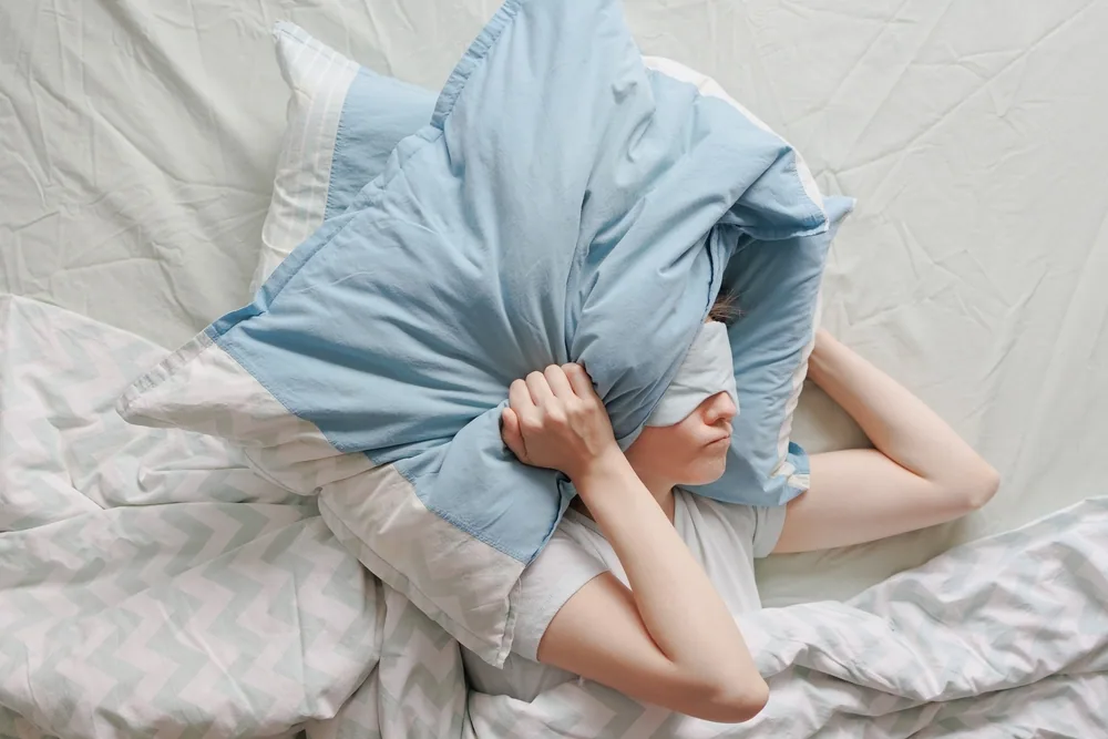 布団を頭に被って悩んでいる様子の女性