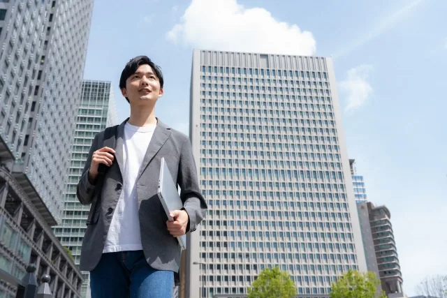 オフィス街をパソコンを持って歩いている若い男性