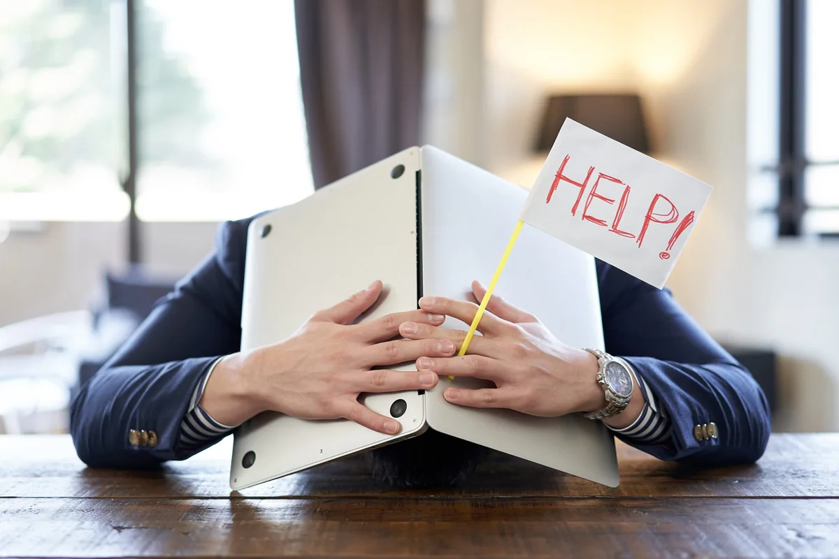 HELPの札を掲げパソコンに伏している男性
