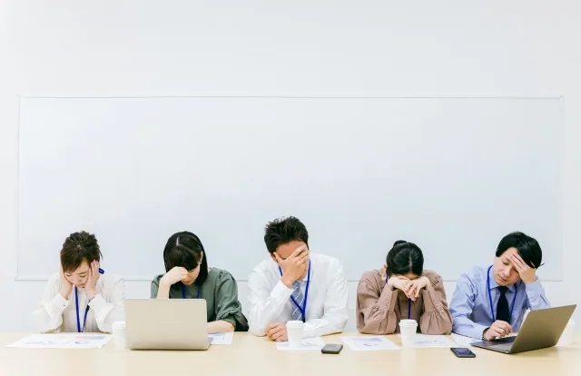 顔を下に向けて悩んでいる様子オフィス内の人たち