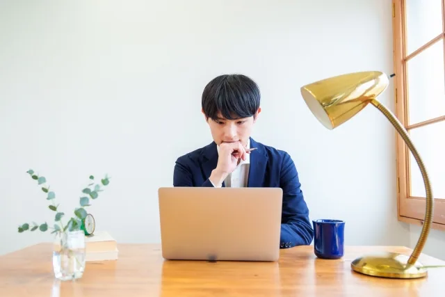 机に向かってPCにて仕事をしている男性