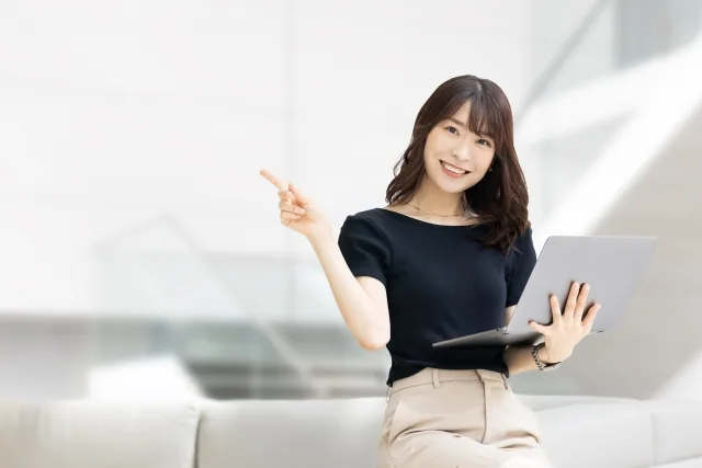 人差し指を上にあげ、パソコンを持っている女性