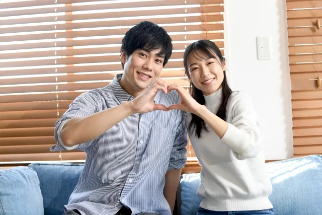 ソファーに座ってハートマークを手で作っている男女