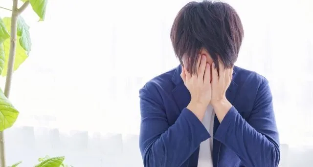 手で顔を覆って悩んでいる男性