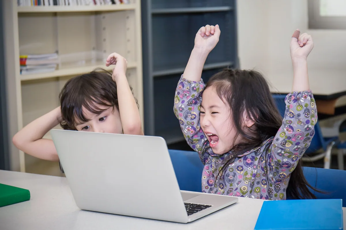 二人の子供がパソコンの前ではしゃいでいる様子