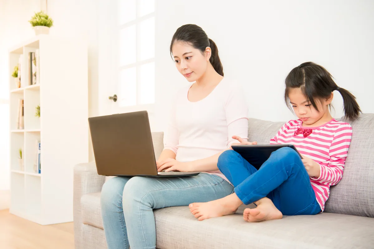子供が遊び母親がパソコンでソファーに座って仕事をしている様子