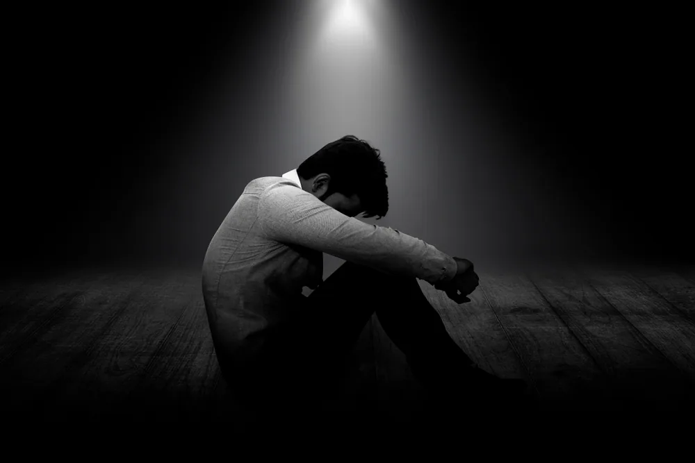 暗い中でスポットライトが当たってうずくまっている男性