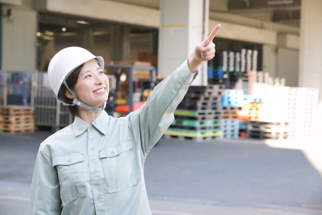 指を空に差し笑顔の作業服の女性