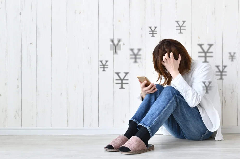 床に座って悩んでいる女性とお金のマーク