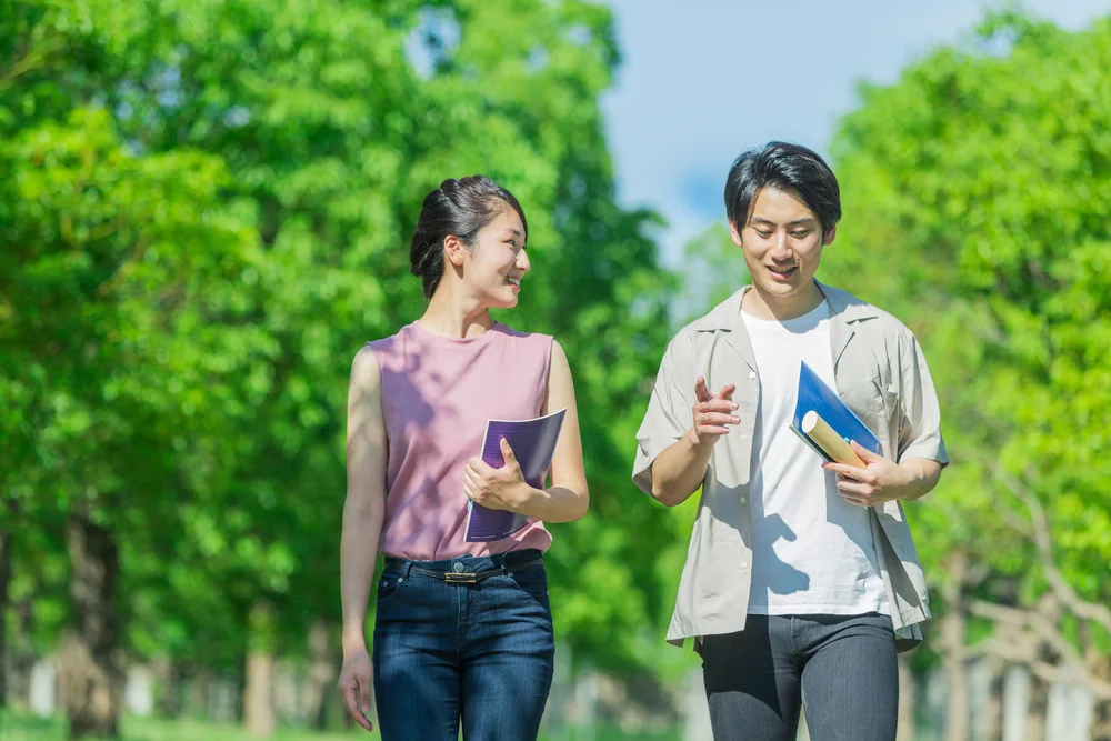 男女がノートやペンを持ちながら外で歩いている様子