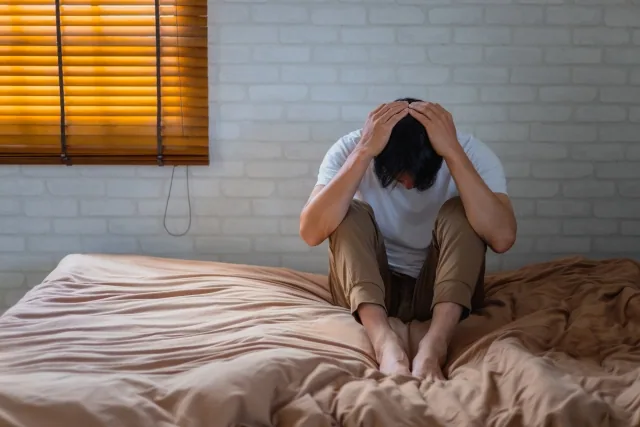 ベッドの上で頭を抱えて悩んでいる男性