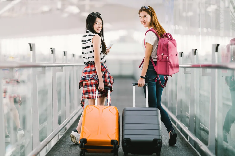 ２人の女性が空港でスーツケースを持って出国する様子