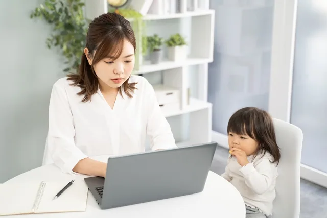 自宅でパソコンで仕事をしている女性とその隣に座っている子供