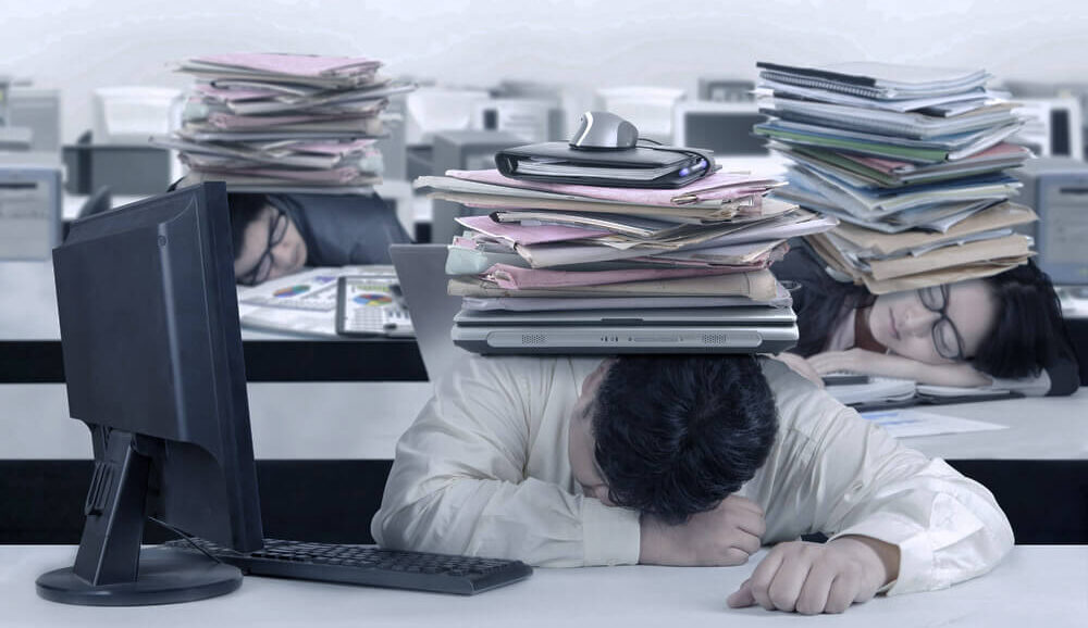 山積みの書類の下の机にうつぶせている人たち