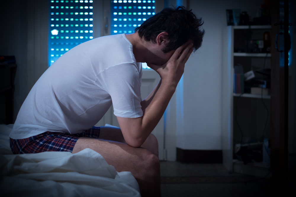 ベッドの上で顔を覆って悩んでいる男性