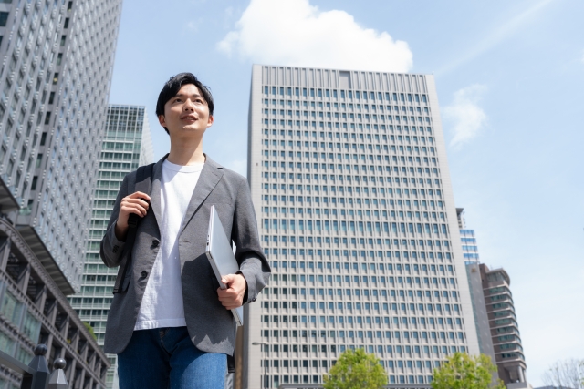 オフィス街をパソコンを持って歩いている若い男性