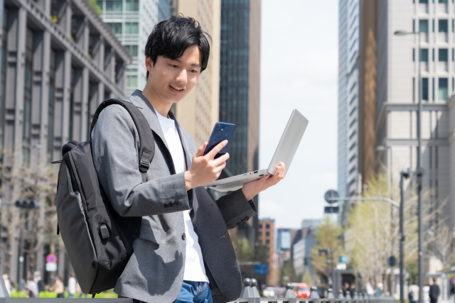 オフィス街でパソコンと携帯を持っている男性
