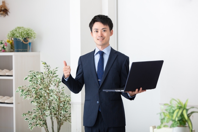 パソコンを持ちながら親指を上げている男性