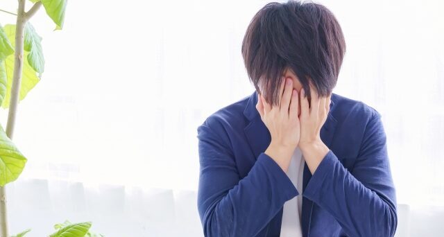 手で顔を覆って悩んでいる男性