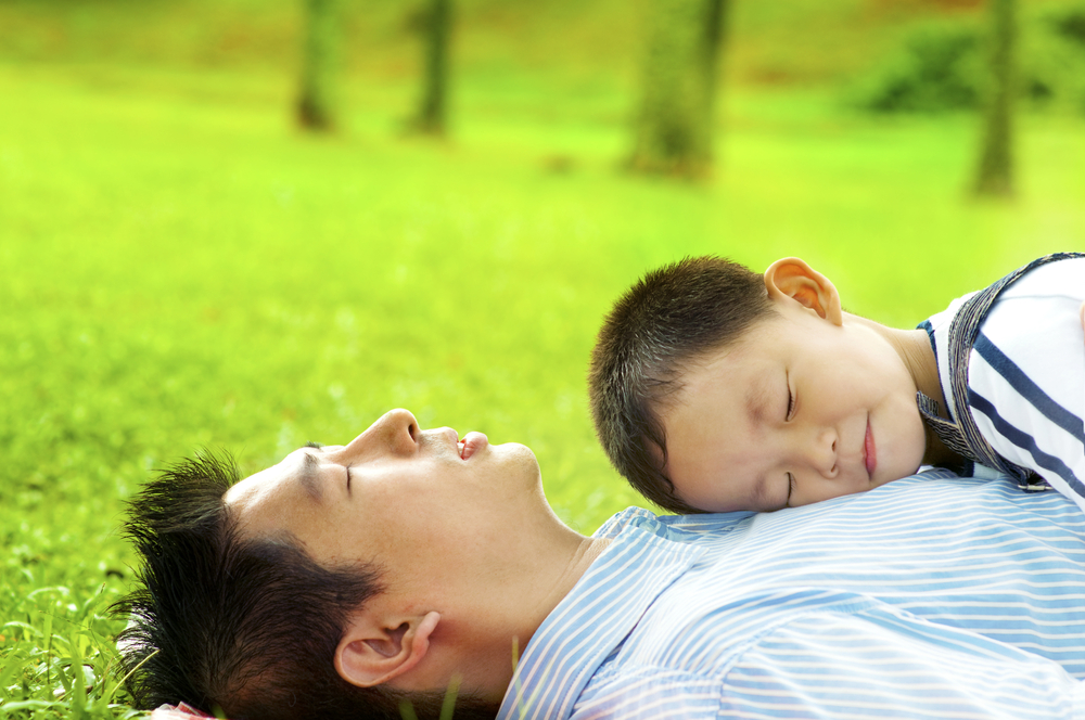 穏やかな表情で芝生に横たわっている父親と小さい子供