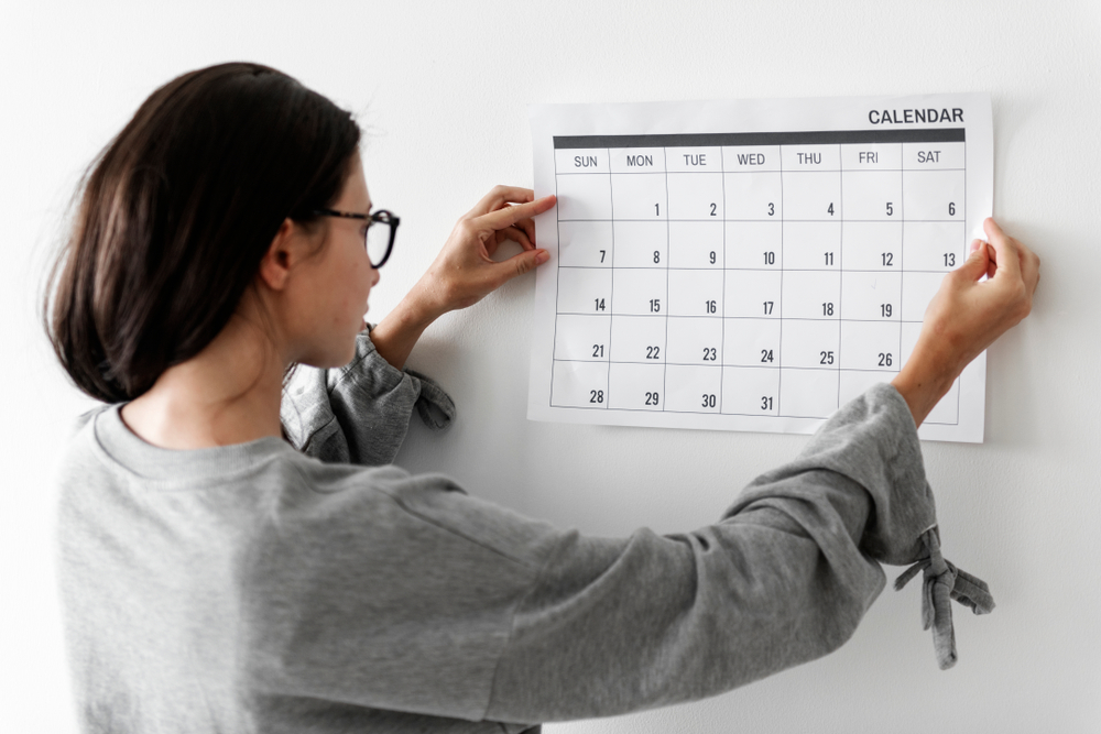カレンダーを壁に貼り見ている女性