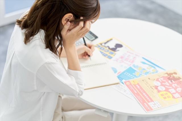 習い事のチラシと計算機を目の前に悩んでいる主婦