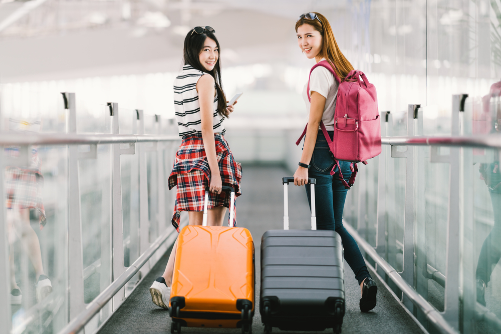 ２人の女性が空港でスーツケースを持って出国する様子