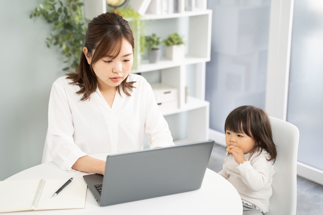 自宅でパソコンで仕事をしている女性とその隣に座っている子供
