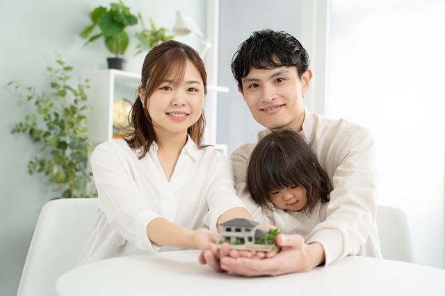 娘を抱えて家の模型を持っている夫婦